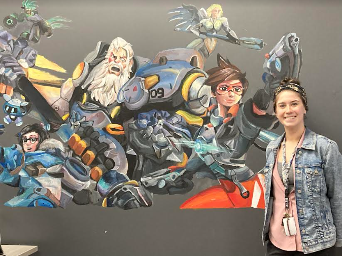 Miss Bousman stands next to the art clubs eSports mural.