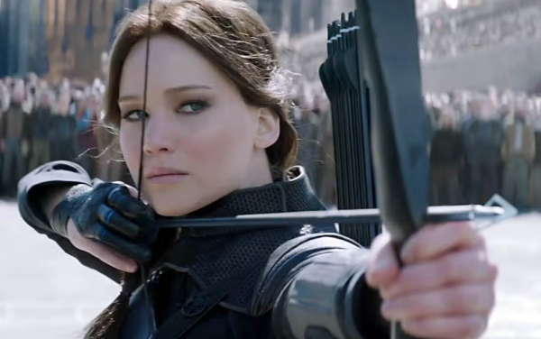 Katniss Everdeen, in a stance holding her bow and arrow ready to shoot. The crowd in the back is waiting for Everdeen to execute the ex-president. 